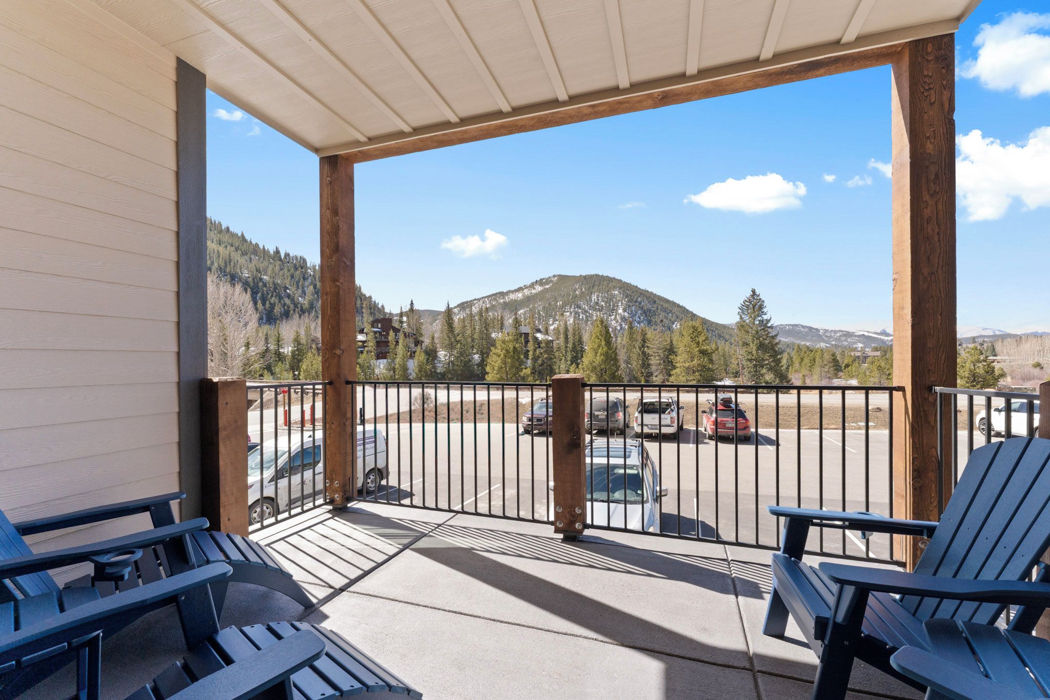 A covered balcony with chairs, a view of a parking lot, and a mountain in the background.