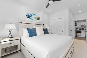 Ein Schlafzimmer mit einem Bett, Nachttischen, einem Deckenventilator und einer Tür, die in eine Küche führt.