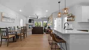 Una cocina moderna con armarios blancos, una isla central, taburetes de bar e iluminación colgante.