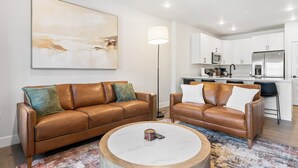 Una sala de estar moderna con dos sofás de cuero, una mesa de centro y una cocina al fondo.