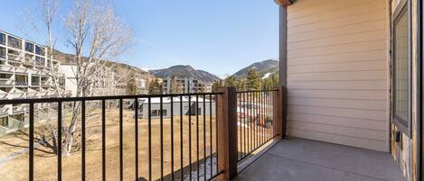 A balcony with a metal railing, a concrete floor, and a view of a mountainous landscape.