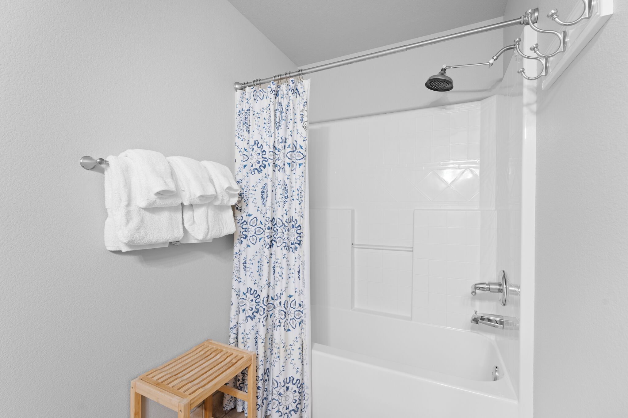 A bathroom with a shower, a towel rack with towels, and a wooden stool.