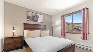 A bedroom with a bed, nightstand, lamp, window with curtains, and a picture on the wall. - 204efc-2 (Silverthorne)