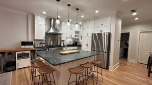Cozinha moderna com ilha central, banquetas, eletrodomésticos de aço inoxidável e iluminação pendente.