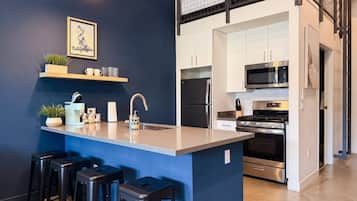 A modern kitchen with a central island, bar stools, and a microwave.