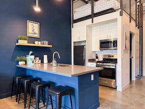 A modern kitchen with a central island, bar stools, and a microwave. - Studio Loft 5 Miles to Disney & Airport w/ Gym (Santa Ana)