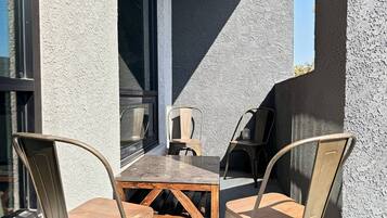 An outdoor seating area with a table and chairs, a window, and a textured wall.