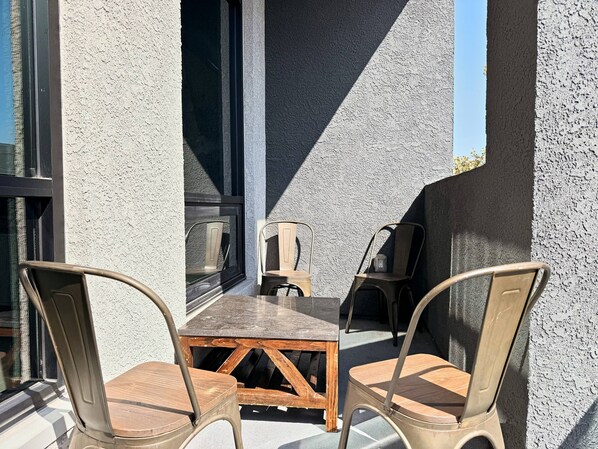 An outdoor seating area with a table and chairs, a window, and a textured wall.