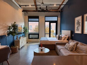 A modern hotel room with a large bed, a sofa, a coffee table, and a view of the city through large windows.