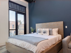 A bedroom with a large bed, a window with a view of buildings, and a potted plant. - Studio Loft 5 Miles to Disney & Airport w/ Gym (Santa Ana)