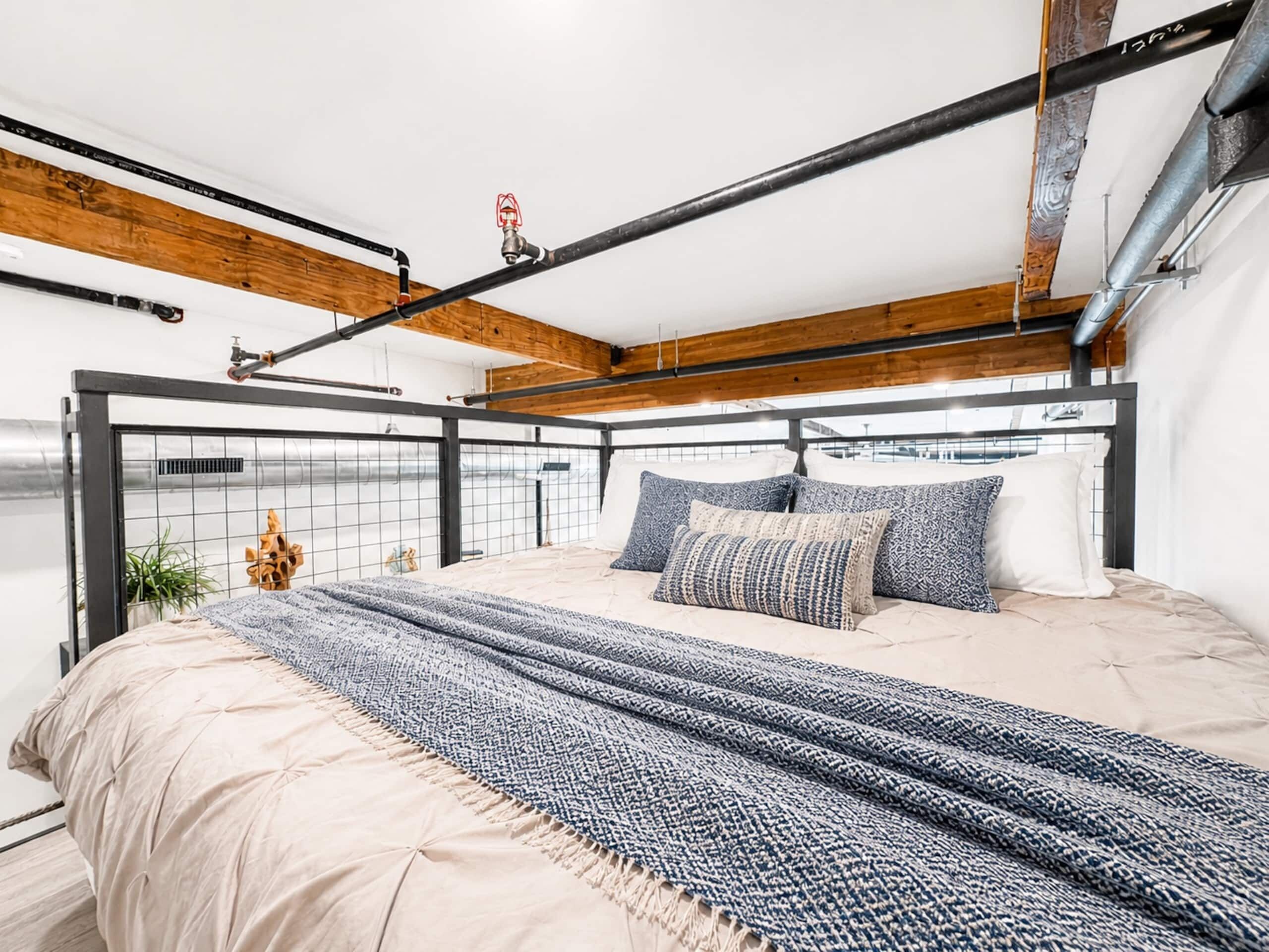 A modern bedroom with a metal bed frame, a wooden ceiling, and a view of the outdoors.