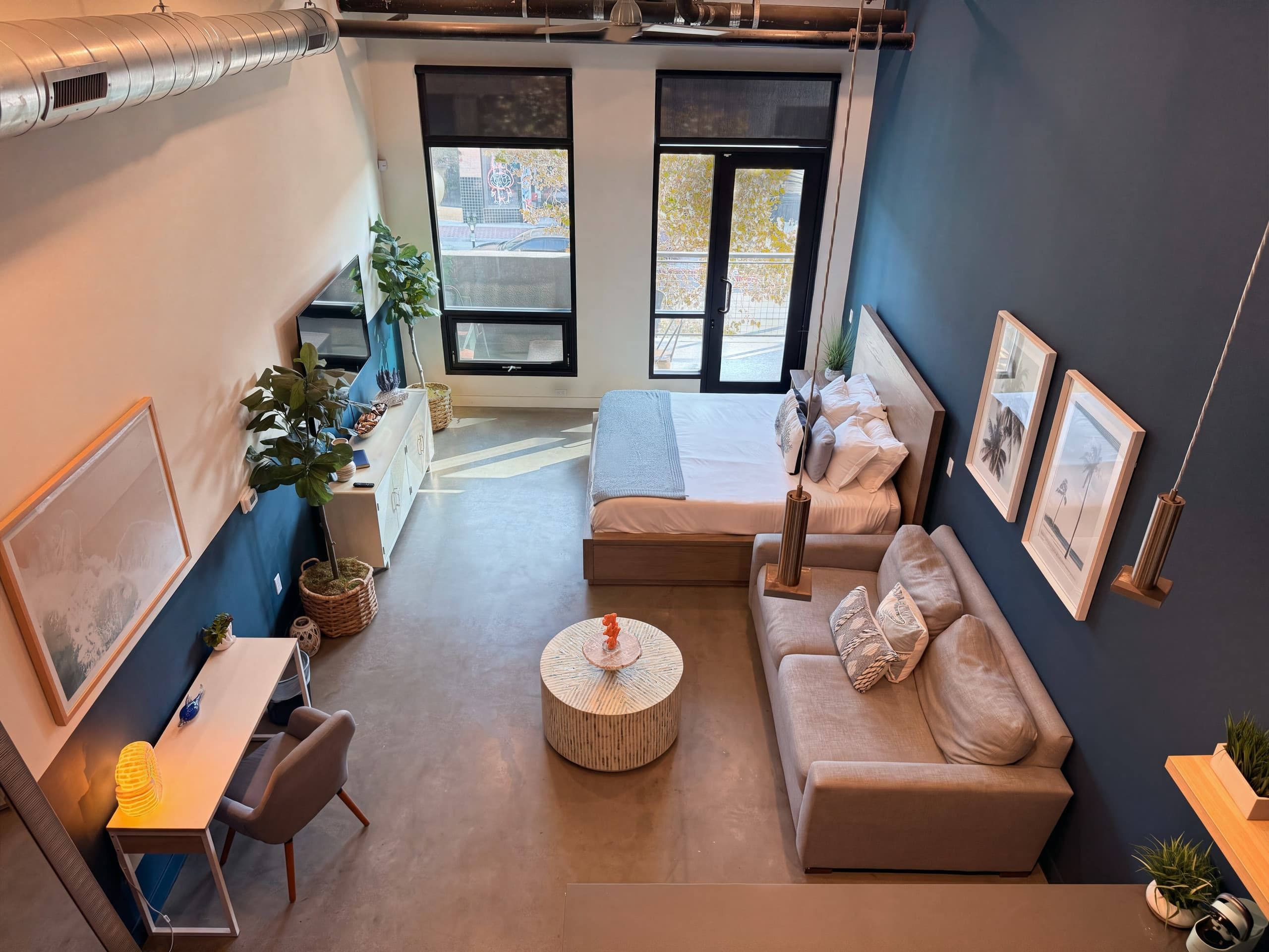 Ein modernes Wohnzimmer mit einer Couch, einem runden Couchtisch, einem Schreibtisch und einem großen Fenster.