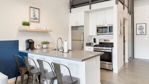 A modern kitchen with a central island, bar stools, a coffee machine, and a hanging light fixture. - 5 Miles to Disney & Airport w/ Gym Pet friendly (Santa Ana)