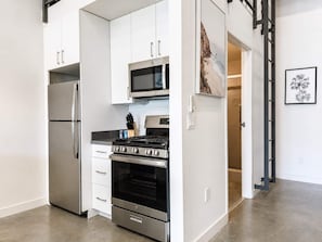 Una cocina moderna con electrodomésticos de acero inoxidable, armarios blancos y un microondas.