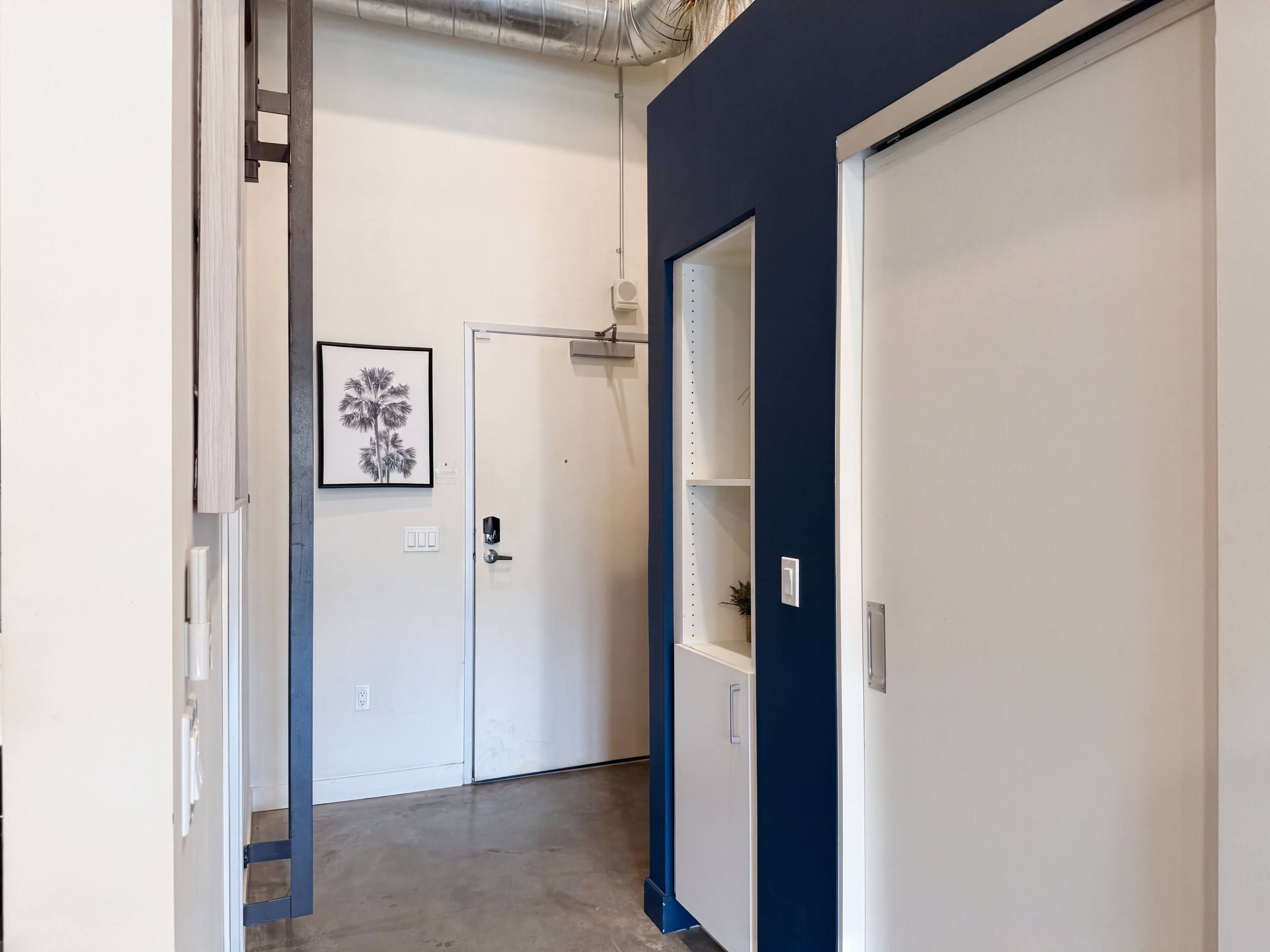 Un pasillo con una puerta blanca, un cuadro en la pared y una pared de acento azul.