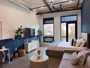 Un dormitorio moderno con una cama grande, un sofá, un televisor y vistas a la ciudad.