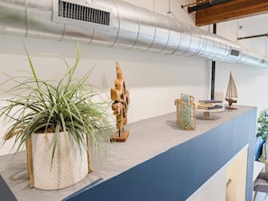 A reception desk with a potted plant, a wooden sculpture, and a wicker basket with books. - Studio Loft 5 Miles to Disney & Airport w/ Gym (Santa Ana)