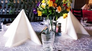 A table set with a white plate, cutlery, and a glass of water, with a vase of flowers in the center. - Nap (Budapest)