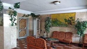 A lobby with patterned sofas, a painting, and potted plants. - Nap (Budapest)