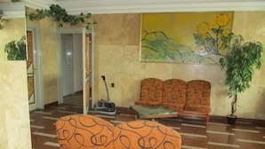 A lobby with patterned seating, a painting, and a potted plant. - Nap (Budapest)