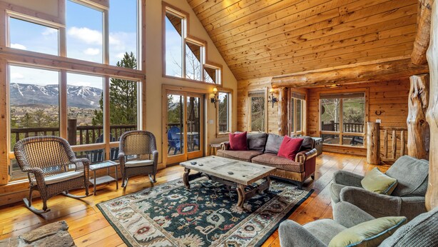 A log cabin interior with a large window, a sofa, rocking chairs, and a coffee table.