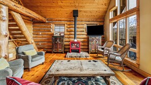 A log cabin interior with a fireplace, wooden walls, a television, and seating.