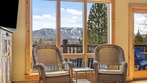 A room with two wicker rocking chairs, a small table, and a large window offering a mountain view.