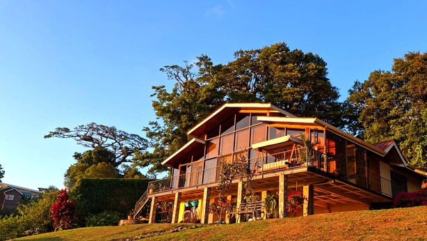 A two-story house with a balcony, surrounded by trees and a grassy slope.