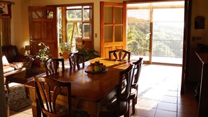 A dining area with a wooden table, chairs, and a view of the outdoors through large windows.