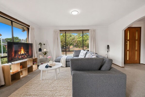 A modern living room with a flat-screen TV, grey sofa, and a small white table.