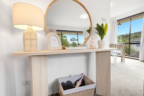 A modern room with a wooden console table, a round mirror, a lamp, and a wicker basket with items.