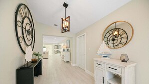Un couloir avec une console blanche, un meuble blanc et une horloge ronde fixée au mur.
