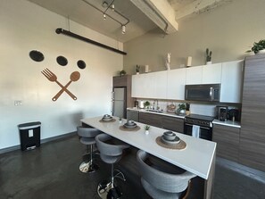 Una cocina moderna con una isla blanca, taburetes de bar, un microondas y un refrigerador.
