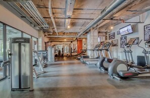 Un gimnasio con equipo de cardio, máquinas de pesas y un espejo grande.