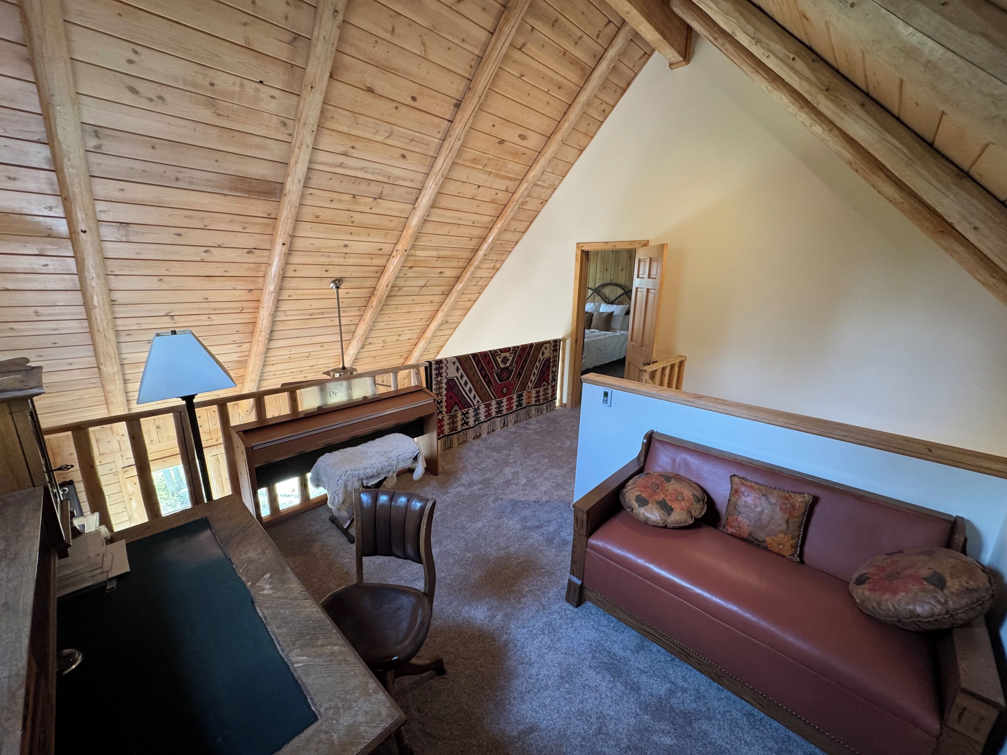 A loft-style room with a sloped ceiling, a wooden desk, a leather sofa, and a small bed.