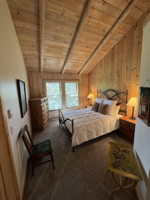 Ein Schlafzimmer mit Holzwandverkleidung, einem Bett, zwei Nachttischlampen, einem Sessel, einer Kommode und einem kleinen Tisch mit einem dekorativen Gegenstand.