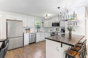 Une cuisine moderne avec des meubles blancs, des appareils en acier inoxydable, un îlot central en bois et un coin bar.