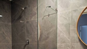 Un baño moderno con cabina de ducha de vidrio, tocador de madera y pared revestida de mármol.
