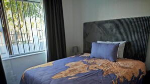 Una cama con una colcha de mapa mundial, un cabecero y una ventana con cortinas.