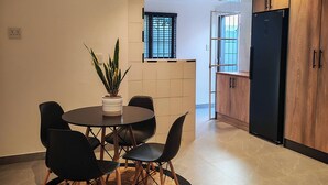 Una cocina moderna con comedor, que incluye una mesa redonda, sillas, una planta en maceta y un refrigerador negro empotrado.