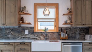 A kitchen with wooden cabinets, a marble countertop, a stainless steel dishwasher, and a pendant light. - Downtown Boulder, Walk Everywhere…Bursting with Charm, Character and Comfort. (Boulder)