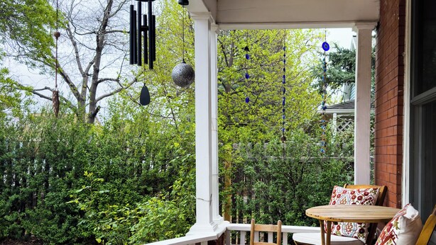 A covered porch with a wooden table and chairs, a woven ottoman, and hanging wind chimes. - Downtown Boulder, Walk Everywhere…Bursting with Charm, Character and Comfort. (Boulder)