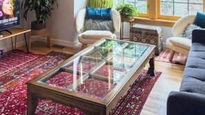 A living room with a ceiling fan, a television, a glass coffee table, two sofas, a patterned rug, and a large window. - Downtown Boulder, Walk Everywhere…Bursting with Charm, Character and Comfort. (Boulder)