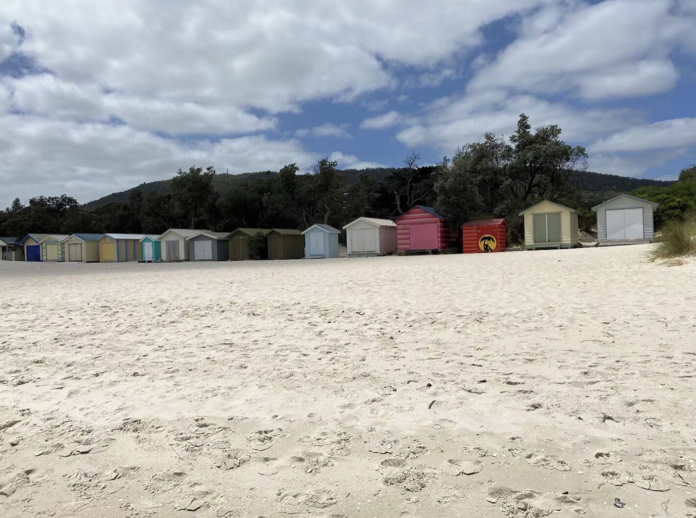 En strand med flere små, farverige strandhuse i række.