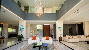 Ein geräumiges, modernes Interieur mit einer zentralen Sitzecke, einer Treppe zu einer oberen Ebene und einer großen Chandelier.