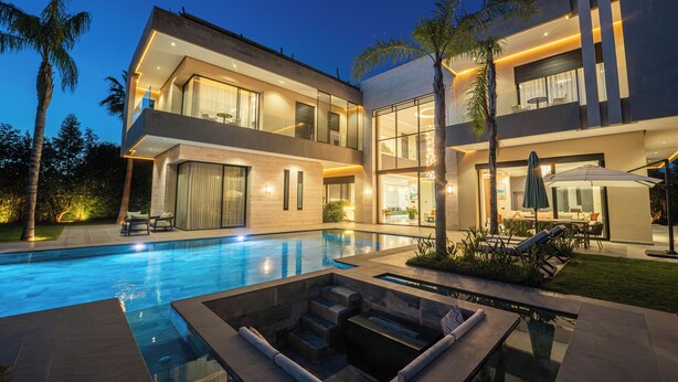 Ein modernes, zweistöckiges Haus mit Swimmingpool, Außenbereich mit Sitzgelegenheiten und einer gut beleuchteten Terrasse.