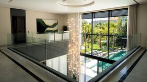 Ein modernes Interieur mit Glastrennwand, Pendelleuchte und Blick auf Pool und Grünflächen.