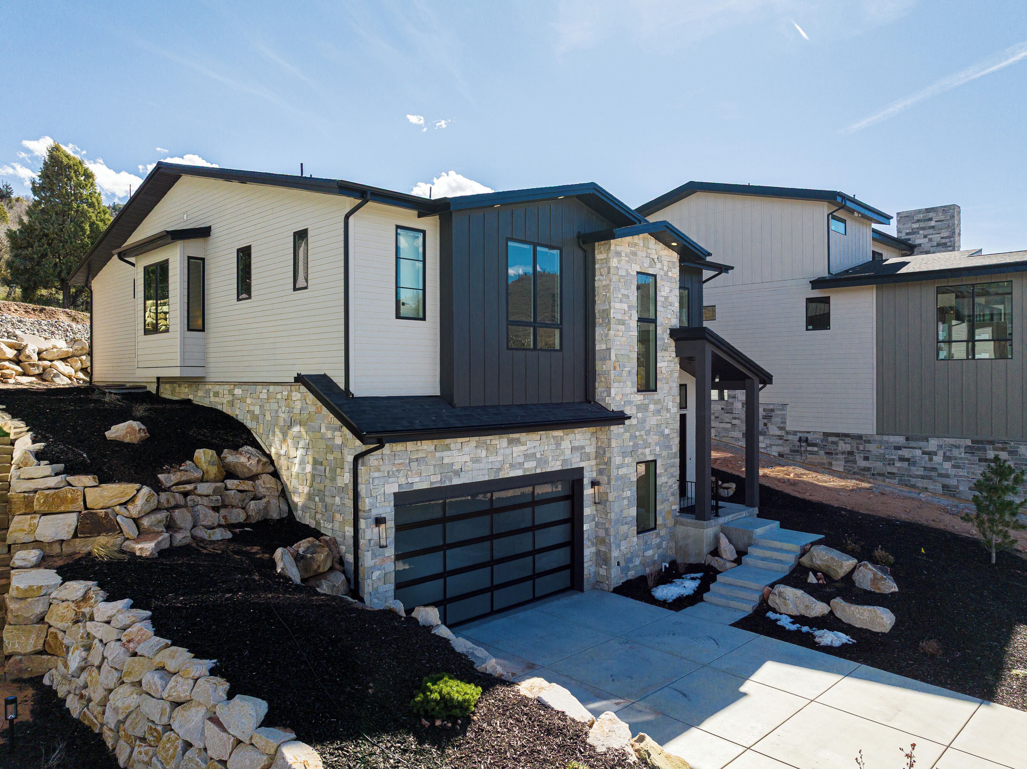 A modern two-story house with a stone facade, a garage, and a landscaped driveway.