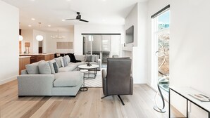 Un salon moderne avec un canapé, un fauteuil et une table basse, une cuisine en arrière-plan et une grande fenêtre offrant une belle vue.