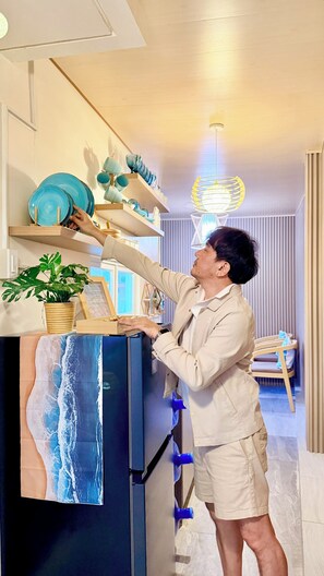 A person arranging blue plates on a shelf in a room with a wooden floor, a potted plant, and a wall-mounted light fixture. - 3-bedroom house in Dauis, Panglao Island, Bohol with cool AC and fitness room (Dauis)